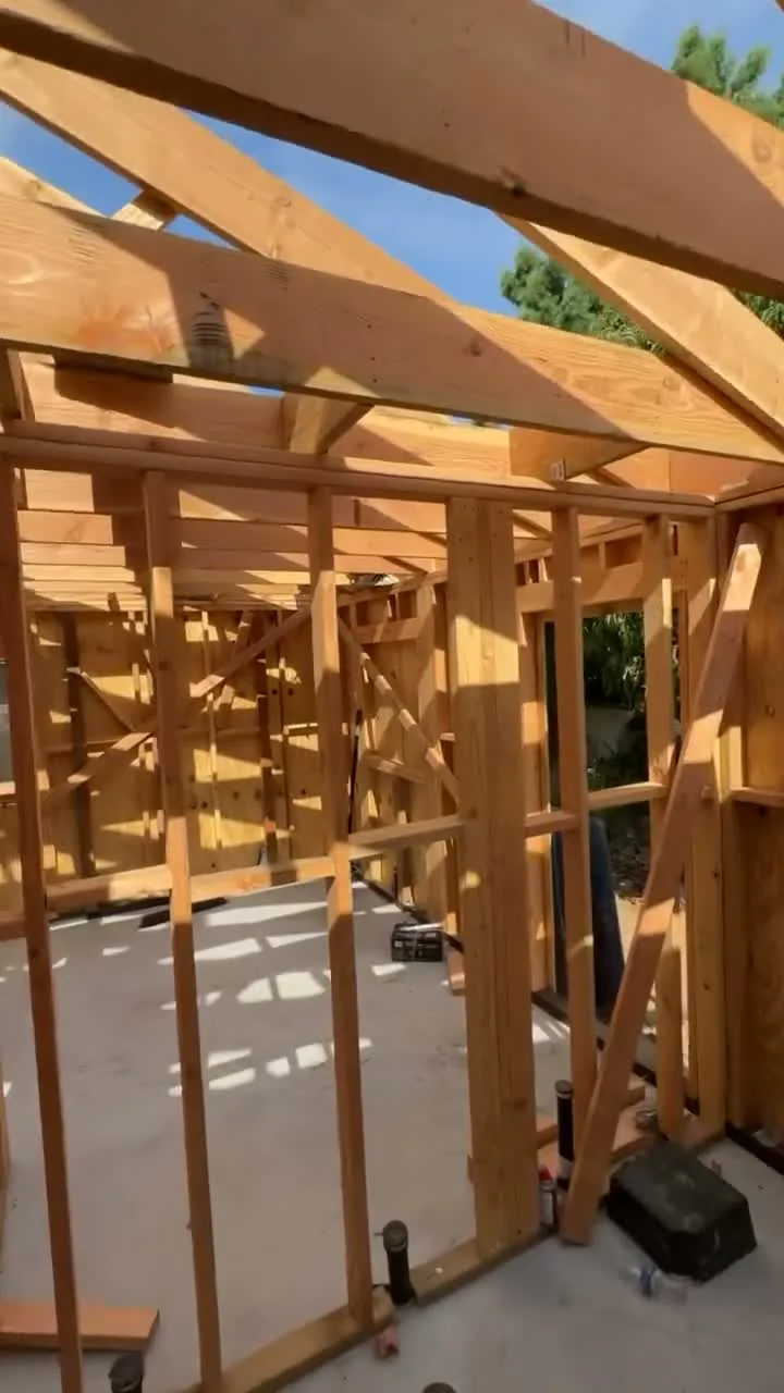 Attached ADU under construction — wall framing and roof rafters against the sky, Orange, Avorino